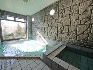 a bathroom with a large tub with a stone wall at Hotel Route-Inn Shimada Yoshida Inter in Shimada