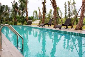 a swimming pool with chairs and palm trees at Porestva Hotel Sriracha in Si Racha
