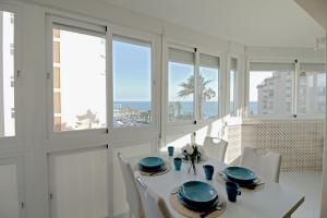 uma sala de jantar branca com uma mesa, cadeiras e janelas em Beach apartment El Faro em Torrox Costa