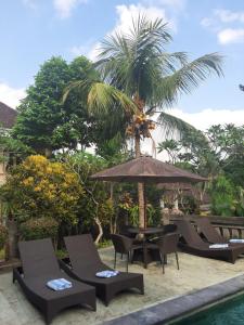 un grupo de sillas y una sombrilla junto a una piscina en Kartika Bungalows, en Ubud