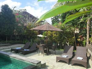 un patio con sillas y una sombrilla junto a la piscina en Kartika Bungalows, en Ubud