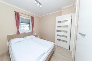 um pequeno quarto com uma cama branca e uma janela em w Akacje Domki nad morzem em Mielenko
