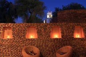 una pared de piedra con luces encendidas con una torre de reloj en Terrantai Lodge, en San Pedro de Atacama