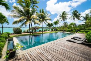 een zwembad in een resort met palmbomen en de oceaan bij Villa 4 chambres THE BAY, pieds dans l'eau au centre de Grand Baie in Grand Baie