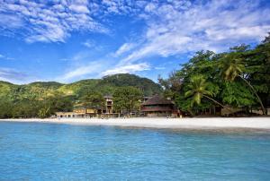 a beach with palm trees and buildings on the shore at Coral Strand Smart Choice in Beau Vallon