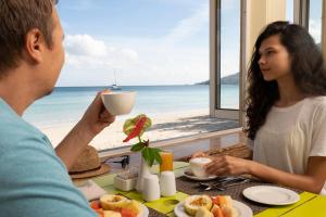 a man and a woman sitting at a table with a cup of coffee at Coral Strand Smart Choice in Beau Vallon