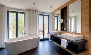 a bathroom with a tub and two sinks and a mirror at Hotel Strandhaus - Boutique Resort & Spa in Lübben