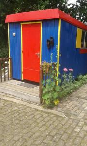 un colorido cobertizo con una puerta roja y algunas flores en De Stadsgaten, en Rouveen