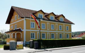 une maison jaune avec un drapeau rouge devant elle dans l'établissement Braugasthof Schmidt`s Rabenbräu, à Neustift an der Lafnitz
