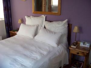 1 cama blanca con almohadas blancas y espejo en Lemontree Cottage, en Heidelberg