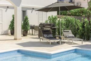 patio z 2 krzesłami i parasolem przy basenie w obiekcie Villa Gala w Trogirze
