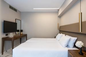 a bedroom with a white bed and a television at Porto Platanias Beach Luxury Selection - Adults Only in Plataniás