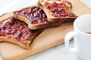 two pieces of toast with jam on a cutting board with a cup of coffee at XOXO Kuta Legian Hostel in Legian +5 photos