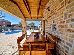 een patio met stenen muren, een houten tafel en banken bij Holiday home Anita 2 for 8 persons with pool in Stankovci