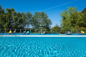 a swimming pool with blue water and chairs and trees at LE SOUFFLE VERT in Cussac