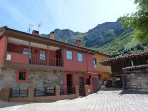 a red building with a balcony and mountains in the background at Casa rural El Tejo in Bermiego