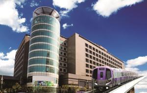 un treno viola su un binario di fronte a un edificio di Fullon Hotel Taoyuan Airport Access MRT A8 a Guishan