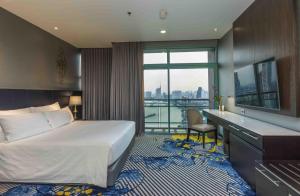 a hotel room with a bed and a desk and a window at Chatrium Hotel Riverside Bangkok in Bangkok