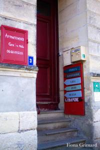un panneau sur le côté d'un bâtiment avec une porte rouge dans l'établissement BUREAUX Appartements LESPARRE MEDOC, à Lesparre-Médoc