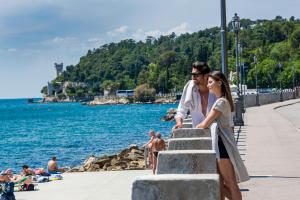 a man and a woman standing on a sidewalk near the water at Hotel Miramare - Adults Only in Trieste