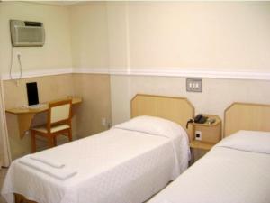 Habitación con 2 camas, escritorio y silla. en Hotel Rosa Mar en Macaé