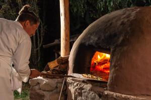 Um homem está a pôr comida num forno. em Casa de La Chola em Ollantaytambo