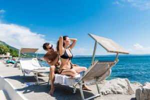 a man and woman in bathing suits sitting on the beach at Hotel Miramare - Adults Only in Trieste