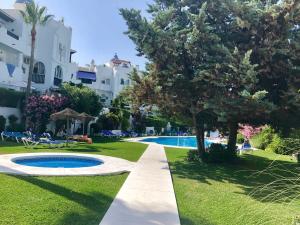 einen Pool in einem Garten mit einem Baum und einem Gebäude in der Unterkunft Bright apartment 300m from the beach in Sitio de Calahonda