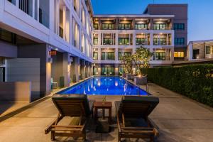 Una piscina con dos sillas y un edificio. en Hotel J Residence Pattaya, en Pattaya central