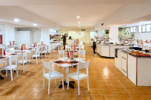 a restaurant with white tables and white chairs and a kitchen at Sol Puerto de la Cruz Tenerife in Puerto de la Cruz