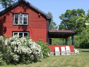 Une grange rouge avec deux chaises blanches devant elle dans l'établissement Two-Bedroom Holiday home in Väddö 1, à Veda