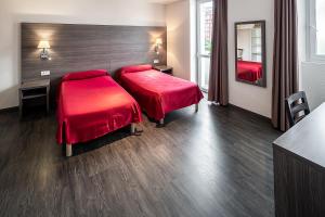 two beds in a hotel room with red sheets at Hôtel Galilée Windsor in Lourdes