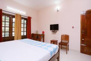 Schlafzimmer mit einem Bett, einem TV und einem Stuhl in der Unterkunft Belhaven Home Stay in Thiruvananthapuram
