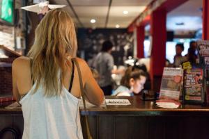 
a woman standing at a counter looking at a cell phone at The Flying Pig Uptown in Amsterdam
