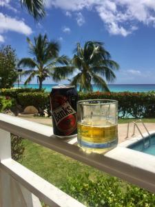 a glass of beer and a can sitting on a railing at Beachfront Apartment in St. Lawrence Gap - Close To Your Every Need in Christ Church