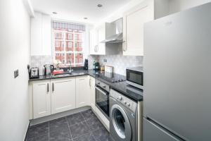 cocina con armarios blancos, lavadora y secadora en Homm - Hyde park 2 bedroom flat, en Londres