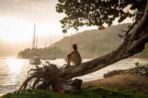 a woman sitting on a tree branch next to the water at Casa Hotel La Mariela in Zapzurro