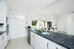 a white kitchen with a black counter top at Blue Zone - Aldinga Beach - C21 SouthCoast Holidays in Aldinga Beach