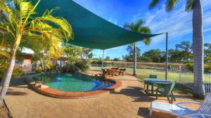 un patio con una piscina con una sombrilla grande en Heritage Lodge Motel, en Charters Towers