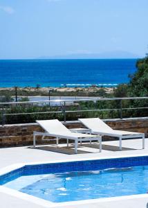 two white benches sitting next to a swimming pool at Dina Naxos Studios in Agios Prokopios
