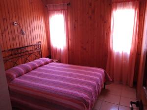 a bedroom with a bed with a striped blanket and two windows at Wooden Nest in Akhladherí
