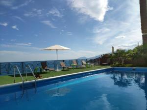 a swimming pool with an umbrella and chairs and the ocean at Guest House Panorama in Malorechenskoye