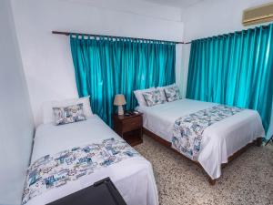two beds in a room with blue curtains at B&M Setup Hotels in Santo Domingo