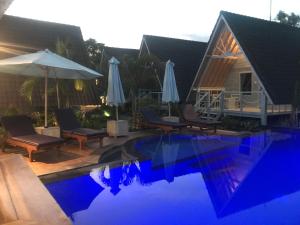 una piscina con sillas y sombrillas junto a una casa en D'Yuki Huts Lembongan, en Nusa Lembongan