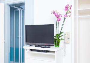 a tv on a white shelf with flowers in a vase at Fábián Panzió in Kecskemét