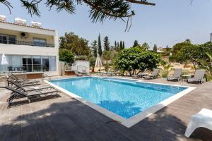 a swimming pool with chairs and a house at Coral Bay Sea Breeze Apartments - 3 Bedroom Apartment in Peyia