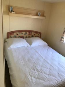 uma cama com lençóis brancos e almofadas num quarto em Caravanverhuur Zeeland em Wemeldinge