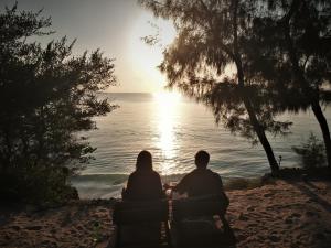 una pareja sentada en la playa viendo la puesta de sol en Seasons Lodge Zanzibar, en Pongwe