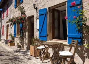 uma mesa e cadeiras em frente a um edifício com persianas azuis em Gîte Rue des Fleurs Puycelsi em Puycelci