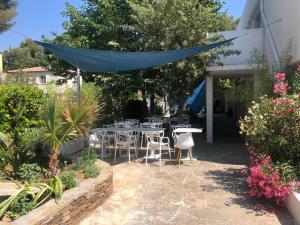 a patio with tables and chairs under a blue canopy at Hotel La Voile in Bormes-les-Mimosas